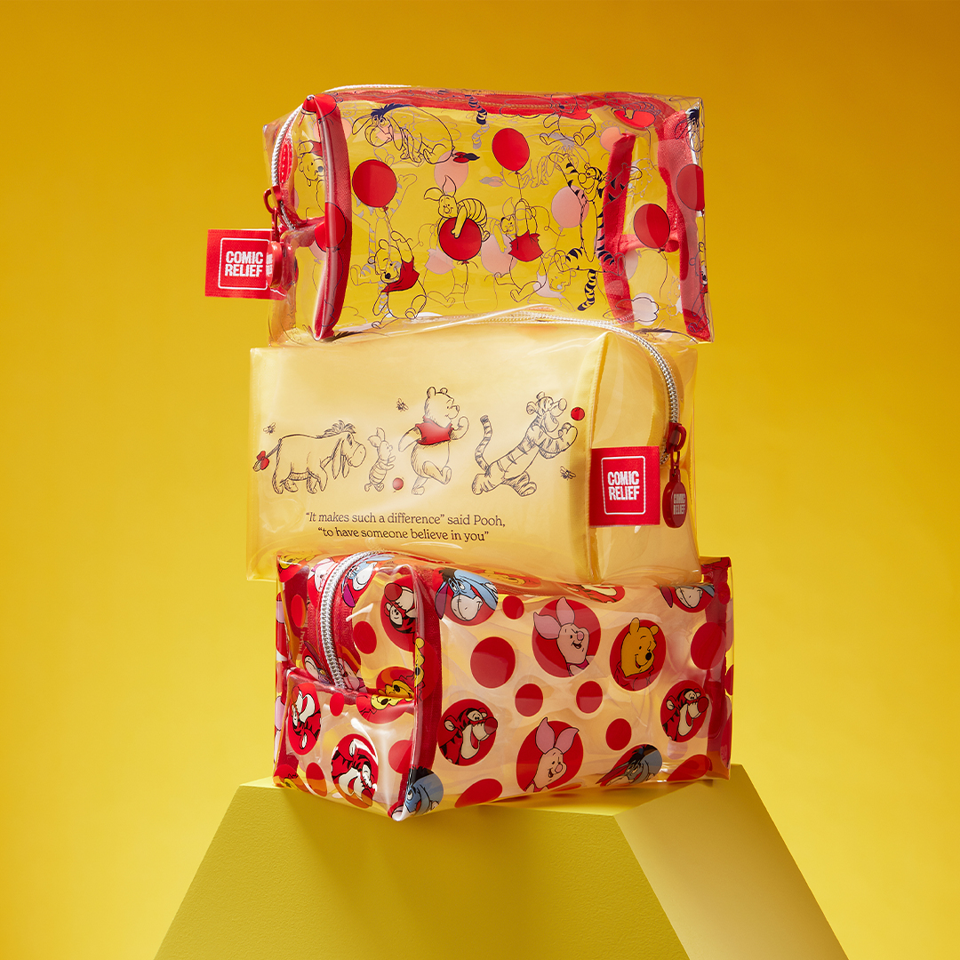 Three Winnie the Pooh–themed cosmetic bags stacked in a pyramid against a bright yellow background. The top bag is clear with red trim and an all over pattern of Pooh and friends with red balloons. The middle bag is soft yellow with an illustration of Pooh, Piglet, Eeyore, and Tigger walking in a line. The bottom bag is red and yellow with a playful polka dot pattern featuring character faces.